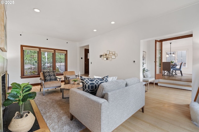 living area with an inviting chandelier, recessed lighting, a tiled fireplace, and light wood-style floors