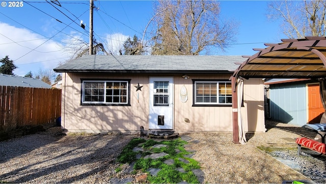 view of front of home with a shingled roof, fence, an outdoor structure, and a pergola