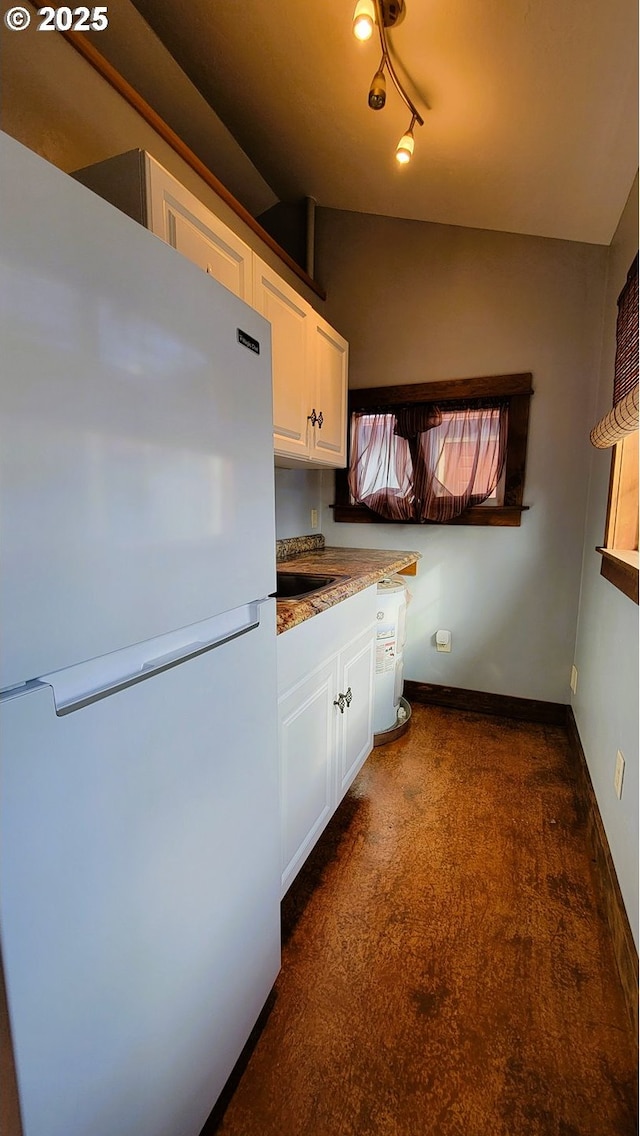 kitchen featuring baseboards, white cabinets, freestanding refrigerator, vaulted ceiling, and a sink