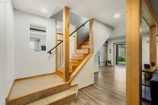 stairs with a wall unit AC, wood finished floors, and baseboards