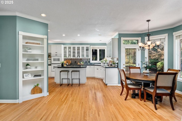 dining room featuring light wood-type flooring, a notable chandelier, crown molding, and a textured ceiling