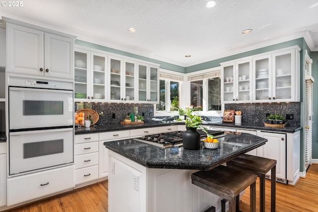 kitchen with light wood finished floors, white double oven, stainless steel gas cooktop, a breakfast bar area, and white cabinetry