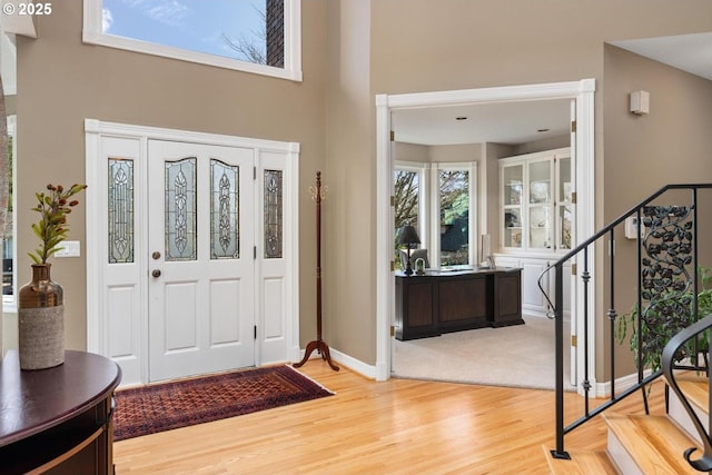 entryway featuring stairs, baseboards, wood finished floors, and a towering ceiling