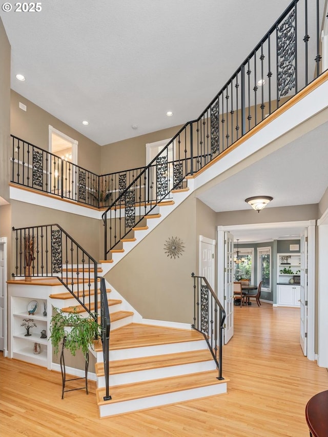 stairs featuring recessed lighting, baseboards, wood finished floors, and a towering ceiling