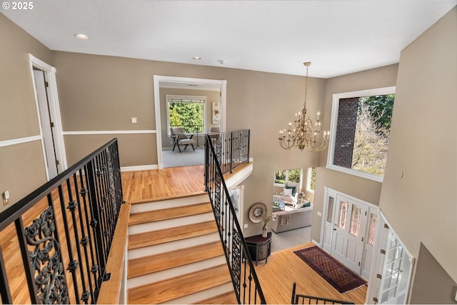 staircase with a wealth of natural light, recessed lighting, an inviting chandelier, and wood finished floors