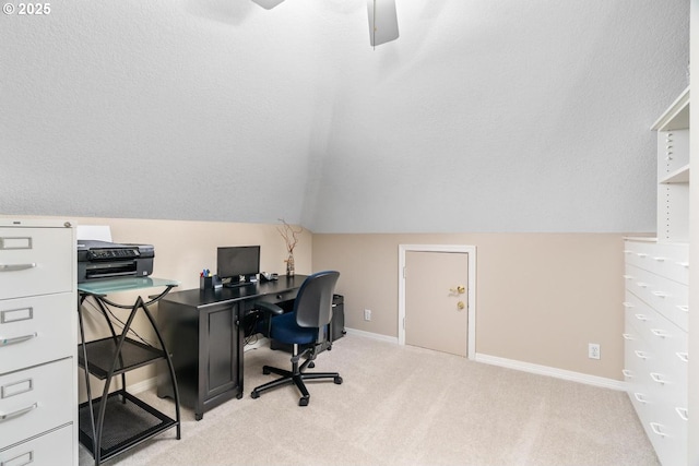 office space with a ceiling fan, baseboards, vaulted ceiling, a textured ceiling, and light colored carpet