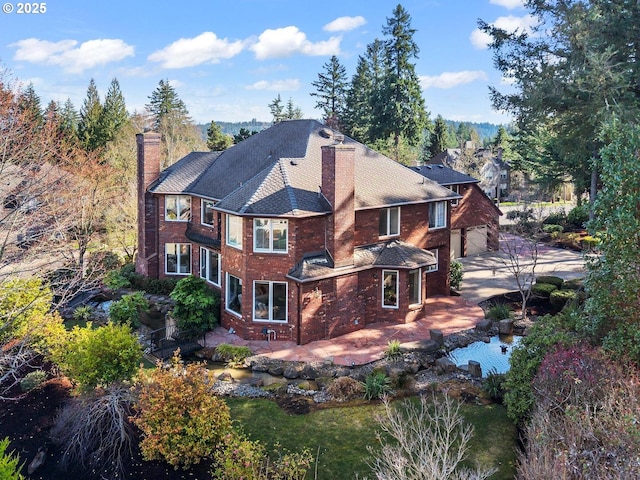 exterior space with a patio, a chimney, concrete driveway, a garage, and brick siding