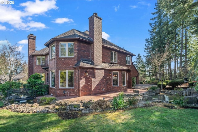 rear view of property featuring brick siding, a lawn, a chimney, a balcony, and a patio