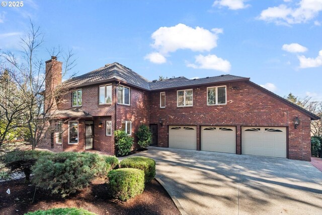 view of front facade featuring an attached garage, brick siding, driveway, and a chimney