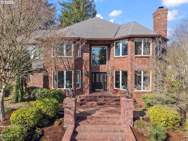 view of front of home with a shingled roof, brick siding, and a chimney