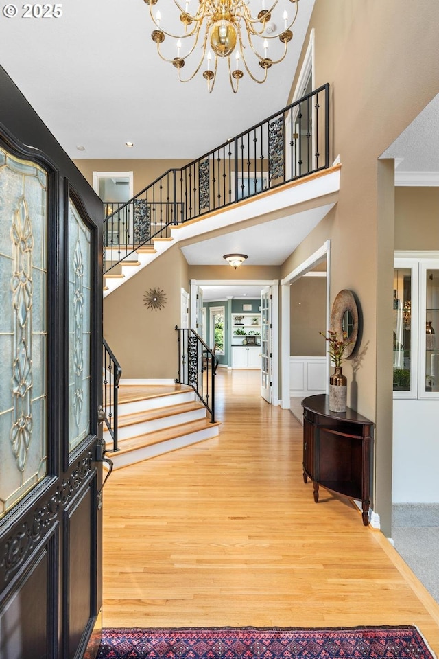entrance foyer featuring light wood-style floors, an inviting chandelier, crown molding, a towering ceiling, and stairs