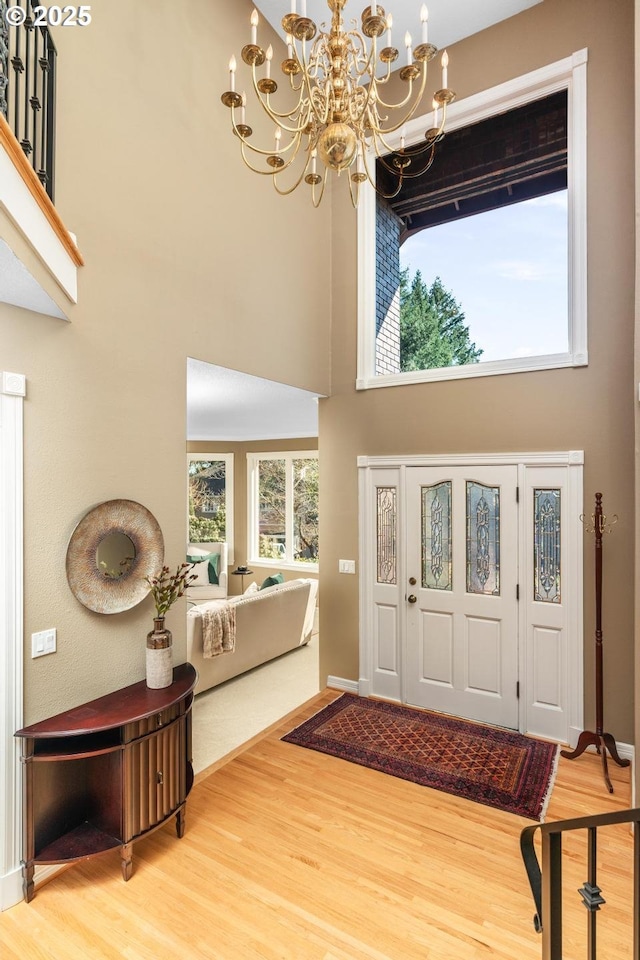 foyer featuring an inviting chandelier, baseboards, a towering ceiling, and wood finished floors