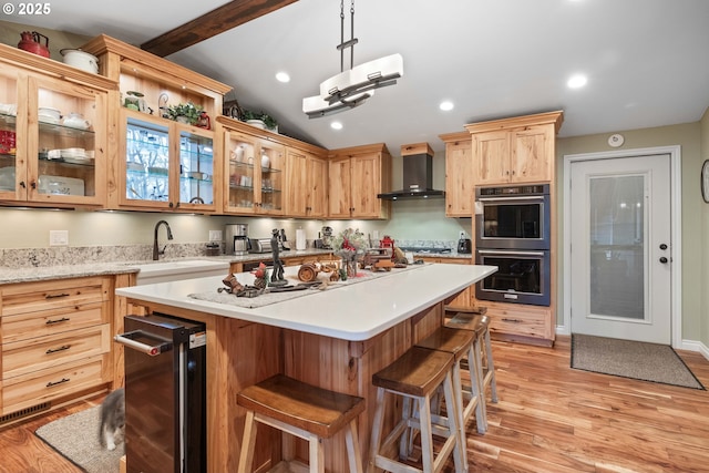 kitchen featuring pendant lighting, stainless steel double oven, wall chimney range hood, and light hardwood / wood-style flooring