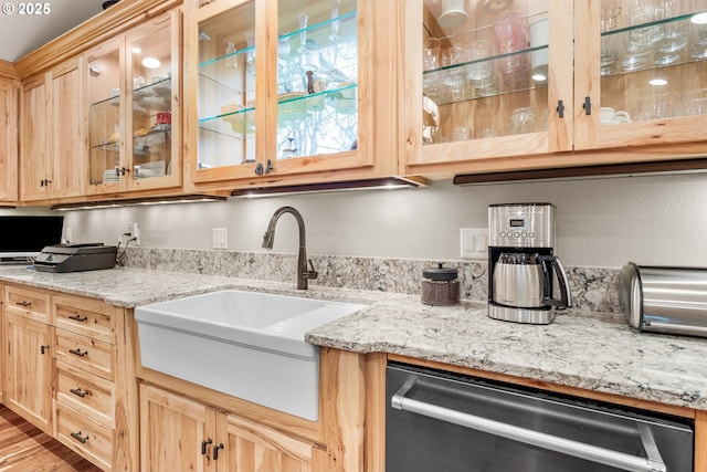 kitchen with light brown cabinetry, light stone countertops, dishwasher, and sink