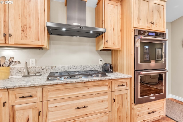 kitchen with light brown cabinets, wall chimney range hood, light stone countertops, wood-type flooring, and stainless steel appliances