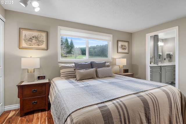 bedroom with a textured ceiling, ensuite bathroom, and light hardwood / wood-style flooring