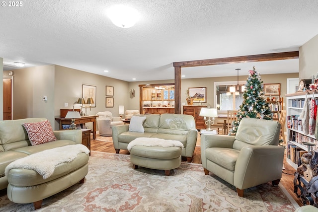 living room with light hardwood / wood-style flooring, beamed ceiling, a textured ceiling, and a notable chandelier