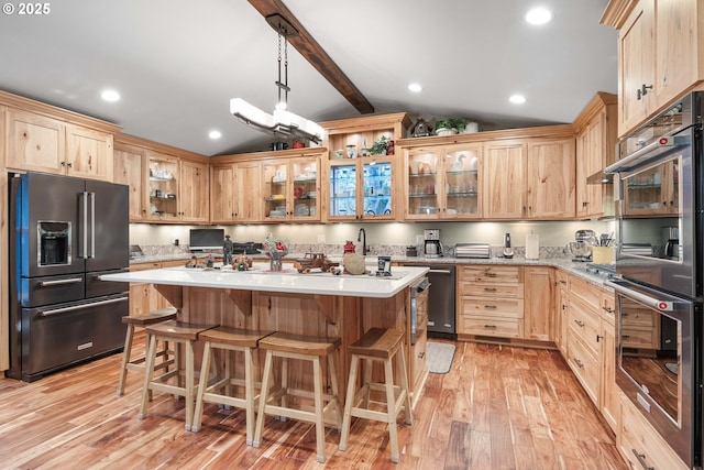 kitchen featuring vaulted ceiling with beams, appliances with stainless steel finishes, pendant lighting, a kitchen island, and light wood-type flooring