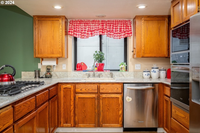 kitchen with appliances with stainless steel finishes, brown cabinets, light countertops, a sink, and recessed lighting