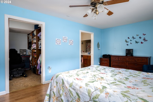 bedroom with a walk in closet, a ceiling fan, connected bathroom, wood finished floors, and baseboards