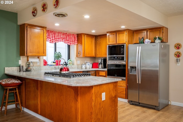 kitchen featuring brown cabinets, visible vents, light wood-style flooring, appliances with stainless steel finishes, and a peninsula