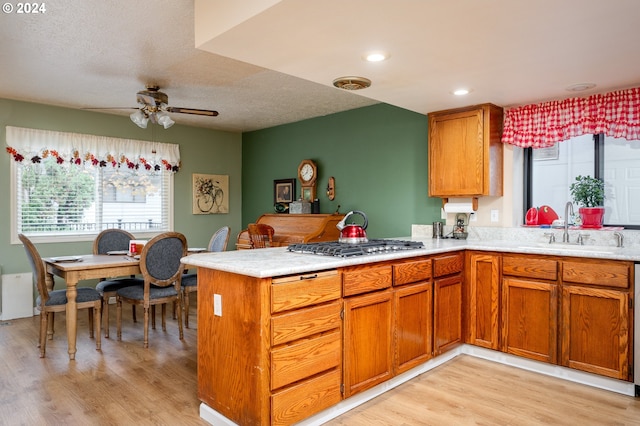 kitchen featuring brown cabinets, light wood finished floors, light countertops, a sink, and a peninsula