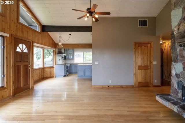 unfurnished living room featuring light wood finished floors, wood walls, ceiling fan, high vaulted ceiling, and baseboards
