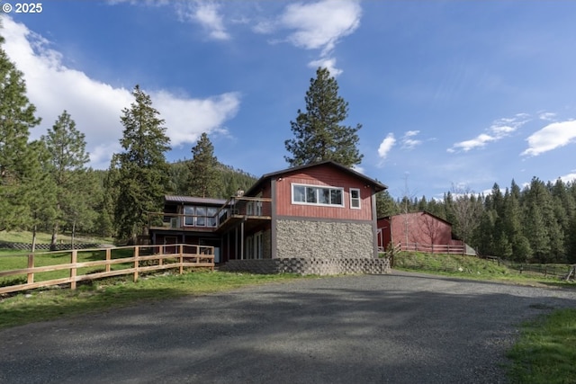 view of property exterior with stone siding, fence, and a wooded view
