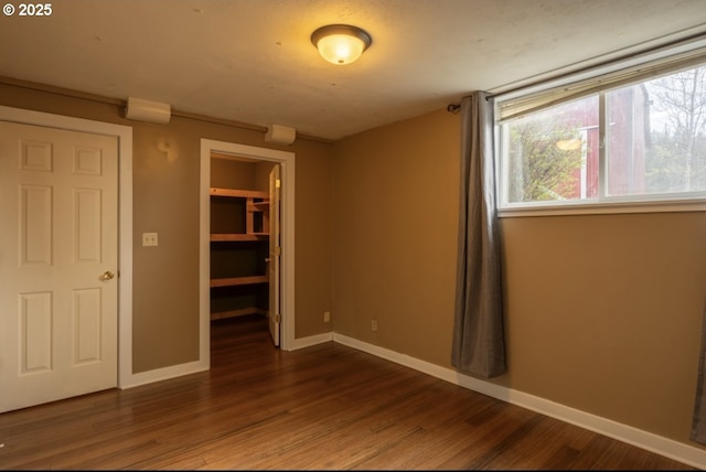 unfurnished bedroom with a closet, dark wood-type flooring, a walk in closet, and baseboards