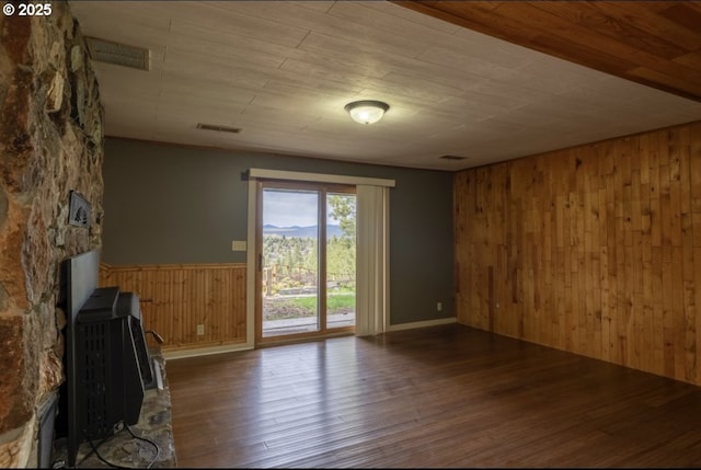 unfurnished living room with wooden walls, wood finished floors, a wood stove, wainscoting, and wood ceiling