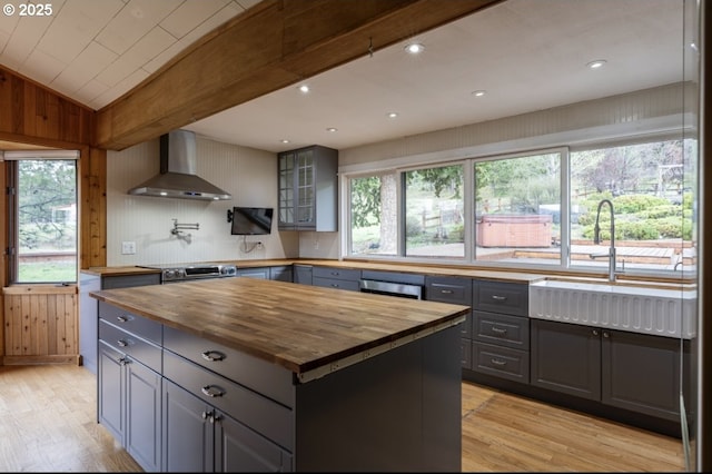 kitchen featuring butcher block counters, wall chimney range hood, gray cabinetry, light wood finished floors, and lofted ceiling