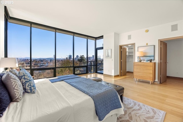 bedroom with hardwood / wood-style flooring, floor to ceiling windows, and a walk in closet