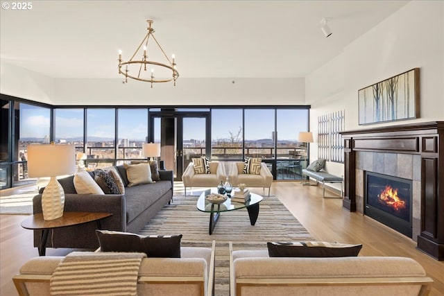 living room with a tiled fireplace, a wealth of natural light, a notable chandelier, and light hardwood / wood-style flooring