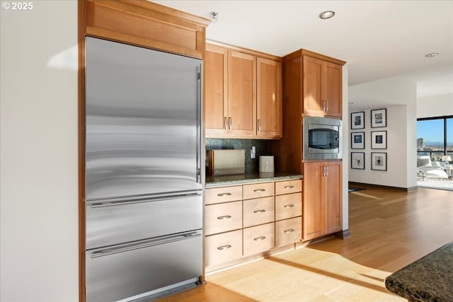 kitchen featuring built in appliances, light wood-type flooring, and dark stone counters