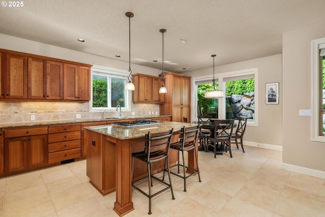 8967 SW 184th Dr, Beaverton, OR 97007 - kitchen with brown cabinets, backsplash, light stone counters, a kitchen island, and stainless steel gas cooktop
