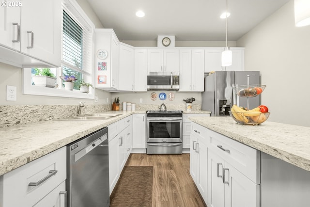 kitchen with appliances with stainless steel finishes, pendant lighting, white cabinetry, sink, and dark hardwood / wood-style flooring