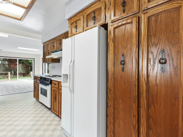 kitchen with light floors, brown cabinetry, under cabinet range hood, and white appliances