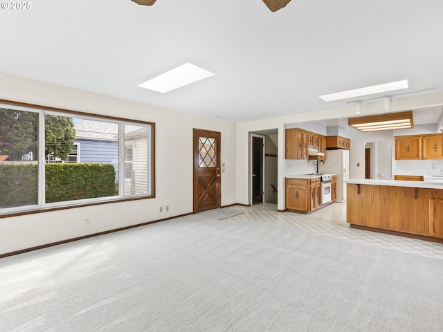 unfurnished living room with a skylight, baseboards, and light colored carpet