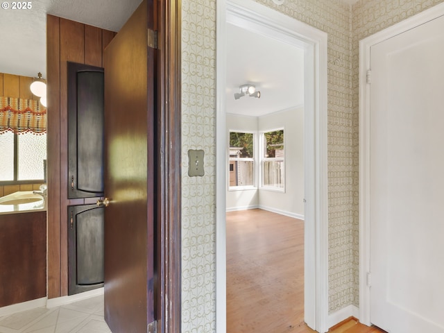 hallway featuring baseboards, light wood finished floors, and wallpapered walls