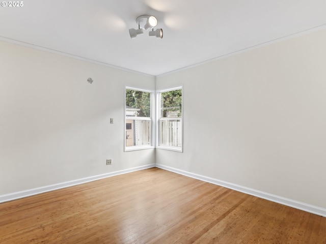 spare room with crown molding, baseboards, and light wood-type flooring