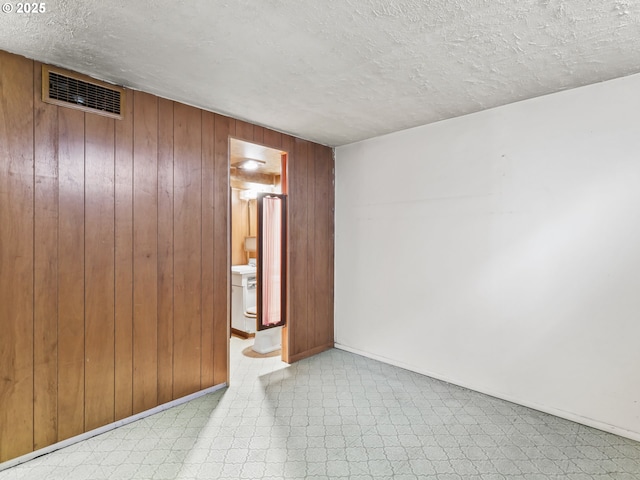 spare room featuring a textured ceiling, visible vents, tile patterned floors, baseboards, and wooden walls