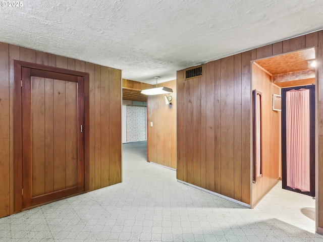 corridor with visible vents, carpet flooring, a textured ceiling, and wooden walls