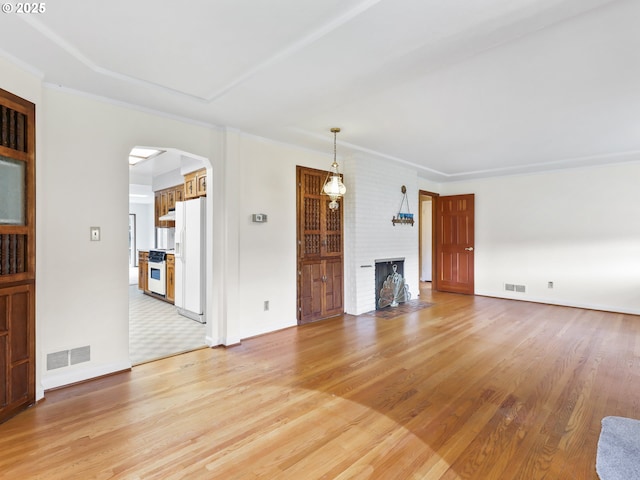unfurnished living room with visible vents, arched walkways, light wood-style flooring, and a fireplace
