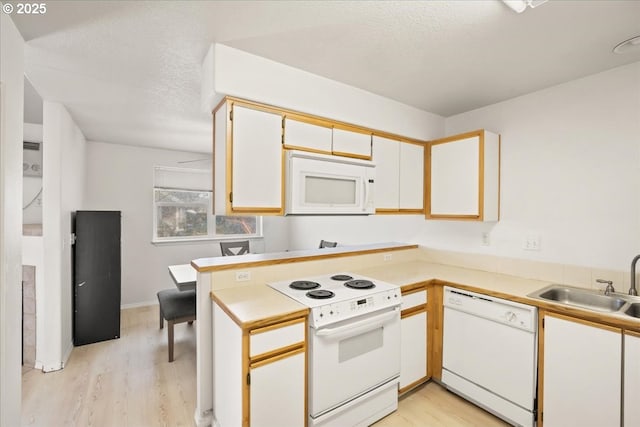 kitchen with light wood-type flooring, a sink, a textured ceiling, white appliances, and a peninsula