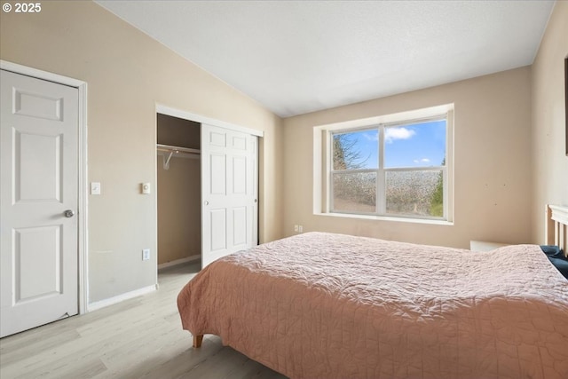 bedroom with a closet, baseboards, light wood-style floors, and vaulted ceiling