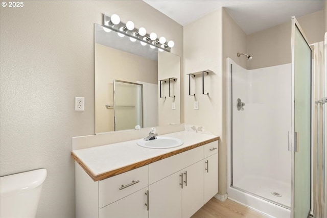 bathroom featuring a stall shower, toilet, vanity, and wood finished floors