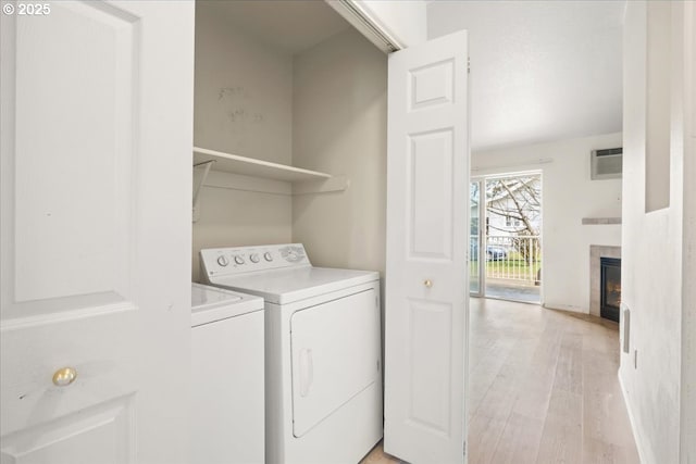 washroom with washing machine and clothes dryer, a tiled fireplace, light wood-type flooring, laundry area, and a wall mounted AC