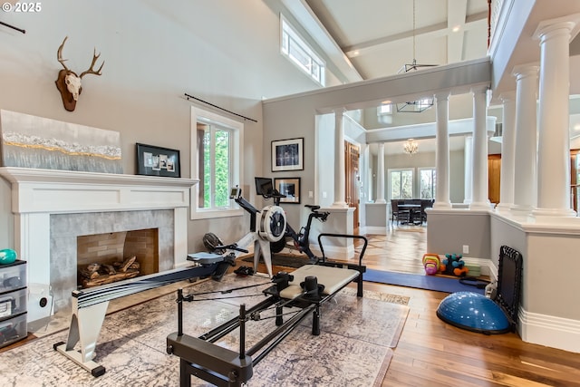 workout area with a chandelier, a premium fireplace, wood finished floors, baseboards, and ornate columns