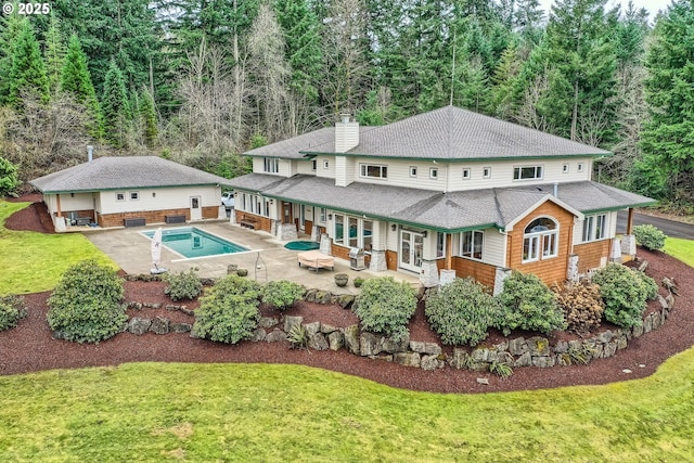 rear view of property with driveway, an outdoor pool, a lawn, a chimney, and a patio area