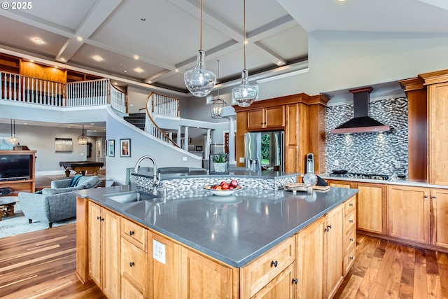 kitchen with wall chimney exhaust hood, dark countertops, a sink, and light wood-style floors